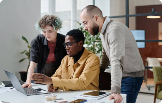 Three colleagues collaborating on a laptop in a modern office setting, focused on their work and sharing ideas.