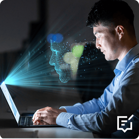 A man sits at a desk using a laptop, which features a face graphic on the screen, as he engages with the device.