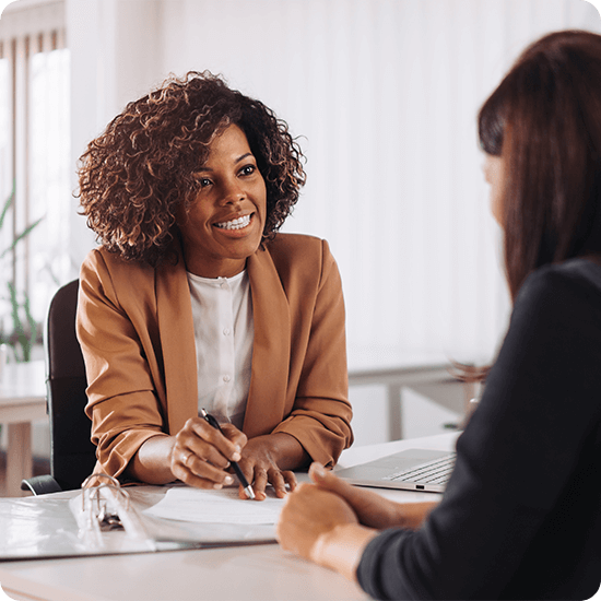 Professional women speaking to each other while seated at a desk